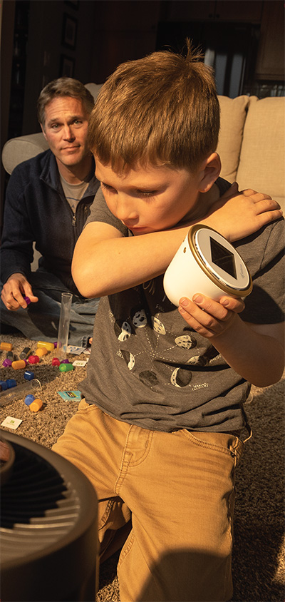 Little boy coughs into his elbow as his father watches from behind him