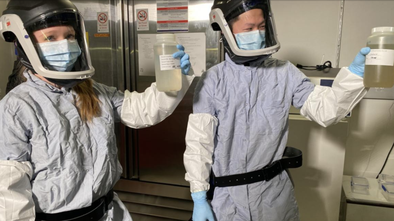 Two graduate students in protective gear hold samples of sewage water