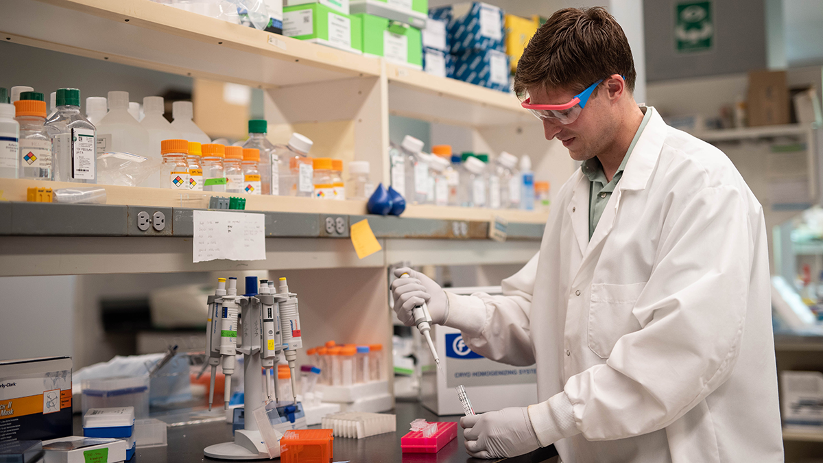Student in a white lab coat working in a lab.