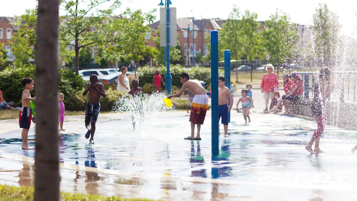 Children play in an urban splash park as adults look on