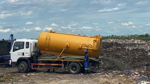 A truck with a large yellow tank empties fecal sludge at a waste site.