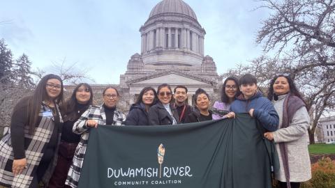 A group of people hold a banner with the logo of the Duwamish River Community Coalition in front of the Washington State capitol building