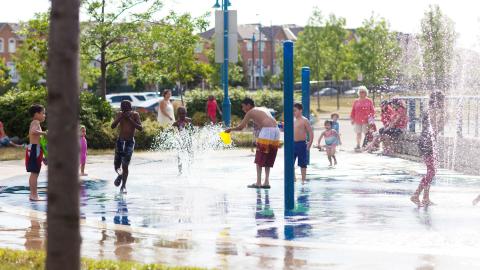 Children play in an urban splash park as adults look on